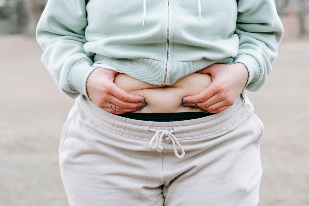 Crop unrecognizable plump woman demonstrating fat on belly